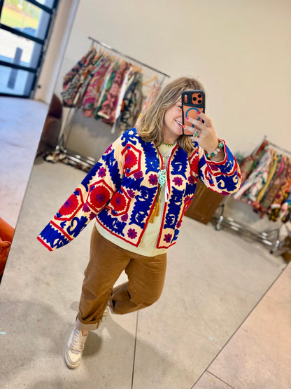 Close-up of the hand embroidery on the Bloom Medallion Jacket, red flowers inside hexagon medallions framed by royal blue and magenta stitching on cream cotton